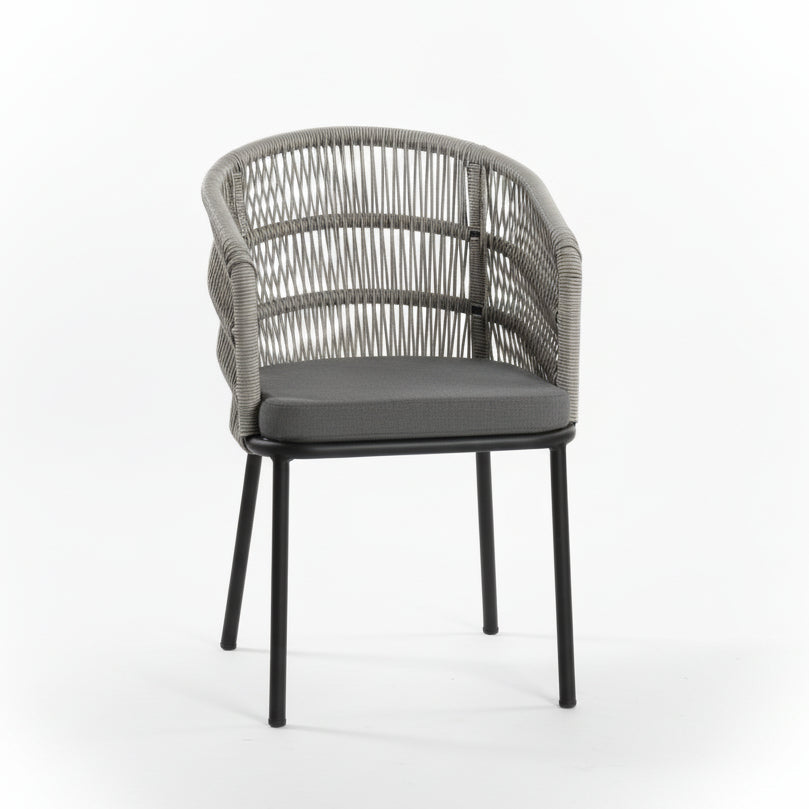 Wicker chair with black cushion on a concrete floor against a white wall.