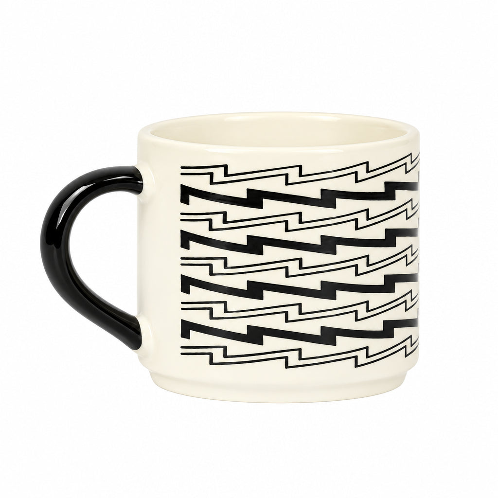 An off-white ceramic mug with a black handle and a black geometric zigzag pattern on the side, set against a plain light gray background.