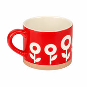 A red ceramic mug with a cream-colored interior and a white floral pattern on the exterior, set against a neutral gray background.