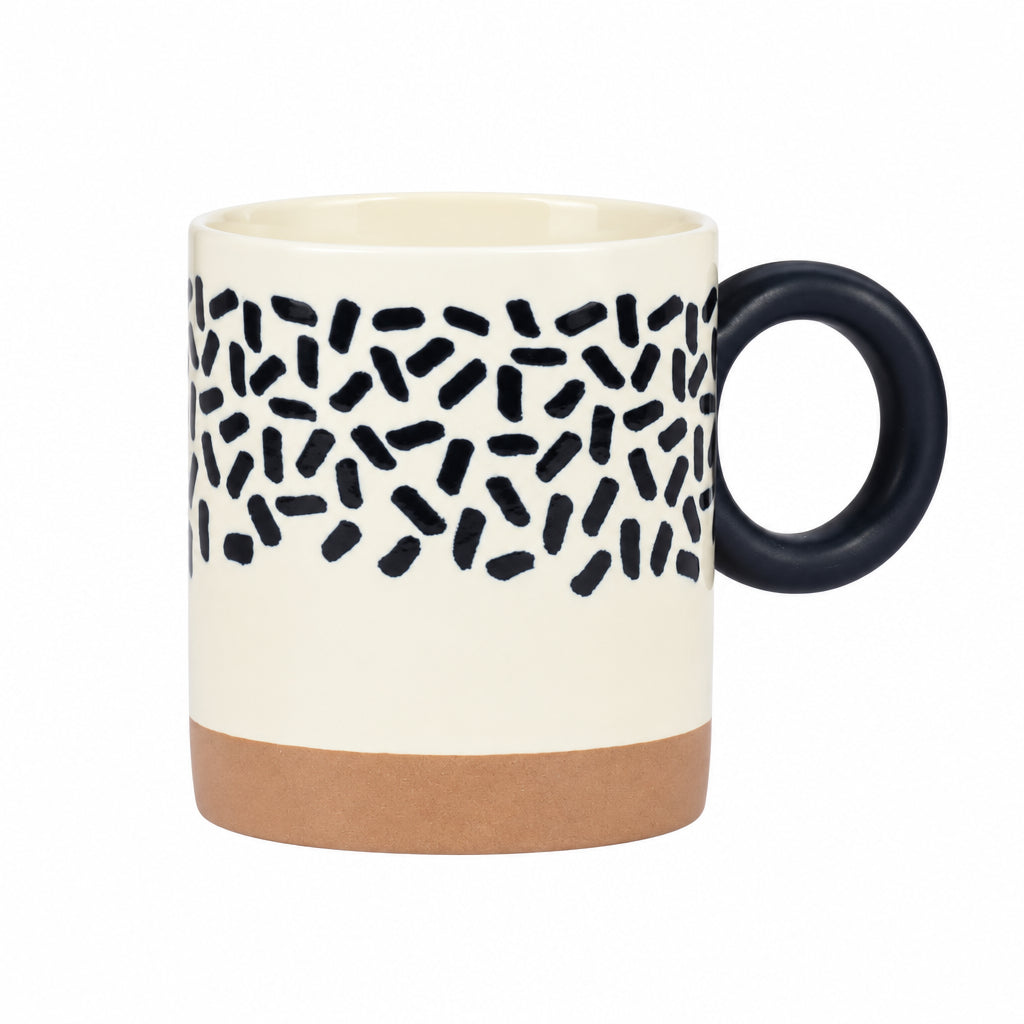 A ceramic mug with a cream-colored body, a black speckled pattern band across the middle, a solid black handle, and a brown base, shown against a light gray background.