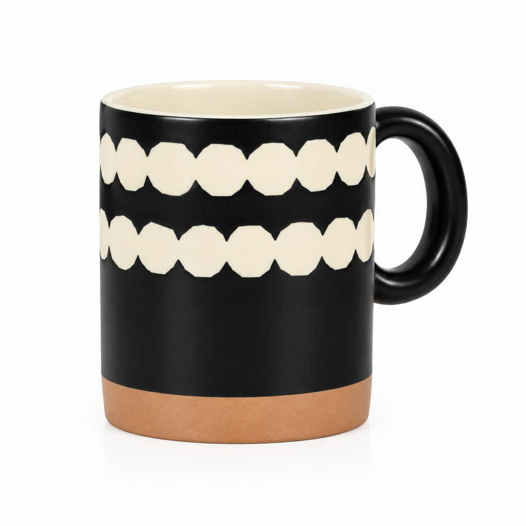 A ceramic mug with a matte black exterior, featuring two horizontal rows of cream-colored geometric teeth-like shapes, a cream-colored interior, and a terracotta-colored base.