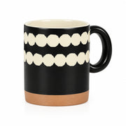 A ceramic mug with a matte black exterior, featuring two horizontal rows of cream-colored geometric teeth-like shapes, a cream-colored interior, and a terracotta-colored base.