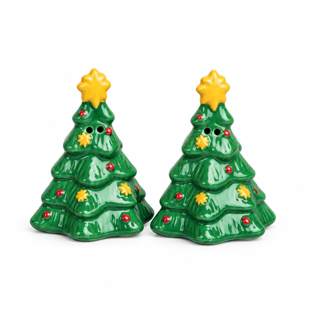 A pair of small green Christmas tree-shaped salt and pepper shakers with gold star toppers, set on a gray stone surface against a textured beige wall.