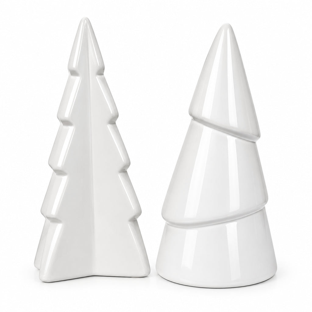 Two white ceramic Christmas tree-shaped ornaments on a wooden desk with papers and a lamp in the background.