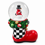 Load image into Gallery viewer, A Christmas-themed snow globe shaped like a red boot, featuring a snowman figure inside a clear globe, green holly, red ornaments, and a black-and-white checkered cuff, photographed on a desk.
