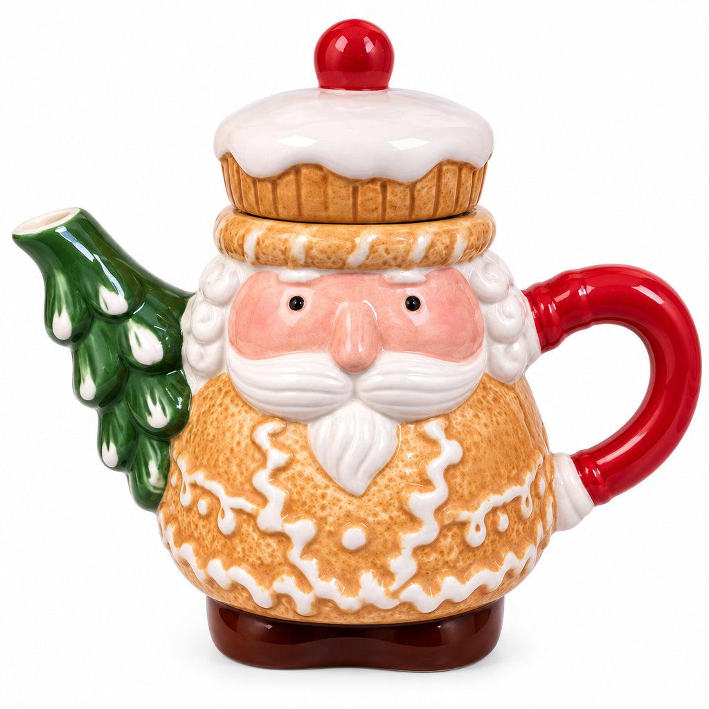 A ceramic Santa Claus holiday teapot shaped like a gingerbread man, with a cupcake lid, red handle, and green Christmas tree spout, resting on bubble wrap in front of a computer monitor.