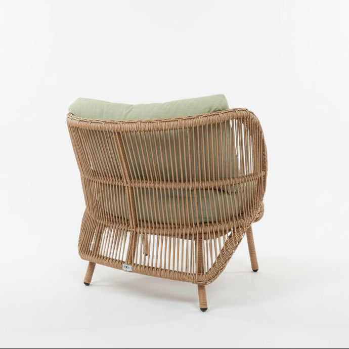 Wicker chair with green cushion on a tiled floor against a white wall.